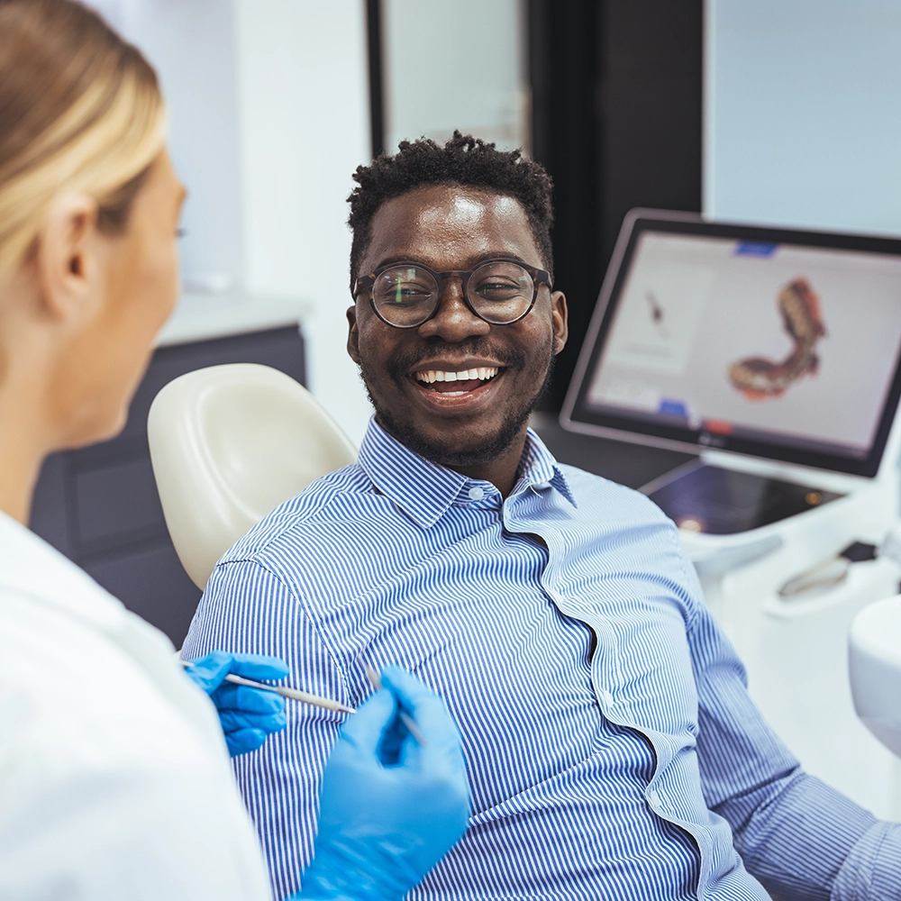 Paciente masculino sonriendo mientras discute tratamientos dentales con una dentista, destacando una experiencia positiva de consulta dental.