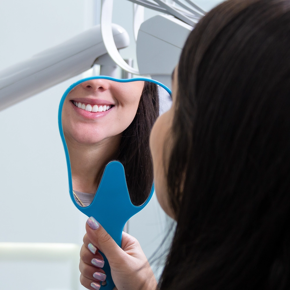 Vista desde atrás de una mujer sonriendo, con su sonrisa reflejada en el espejo que sostiene.