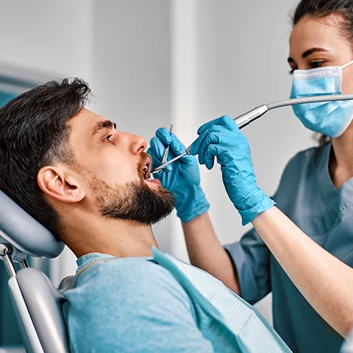 Dentista mujer usando instrumentos dentales en la boca de un paciente masculino.