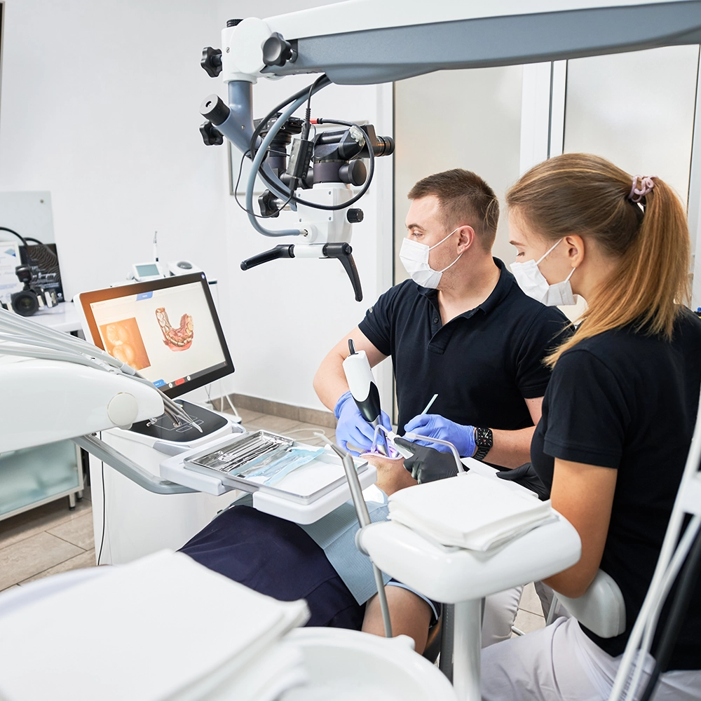 Dentista y asistente dental trabajando con un paciente mientras miran una pantalla.
