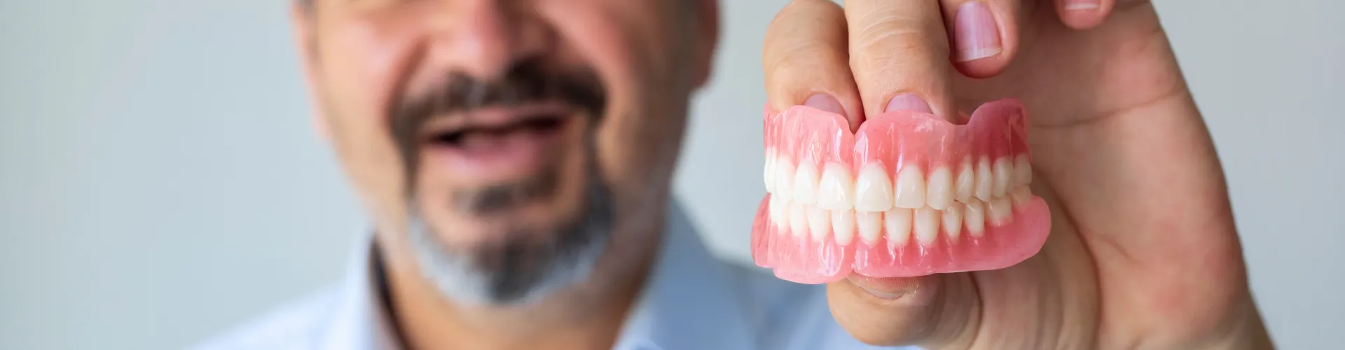 Hombre sonriente sin dientes sosteniendo dentadura superior e inferior.