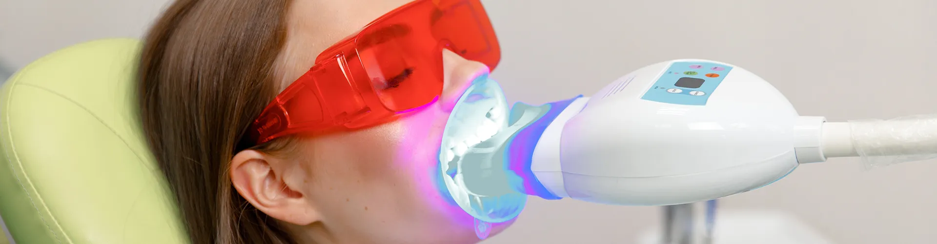 Mujer con gafas naranjas en sillón dental con luz LED en su boca.