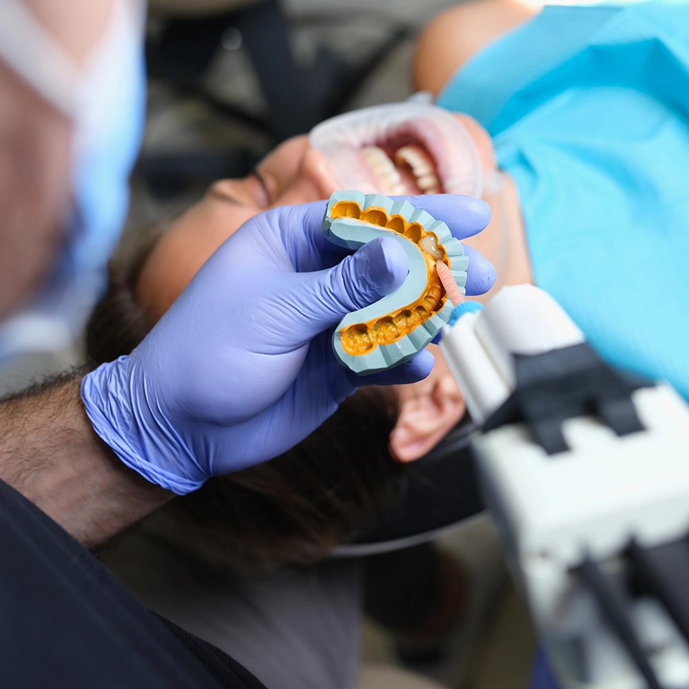 Dentista con guantes azules trabajando con un molde de diente.