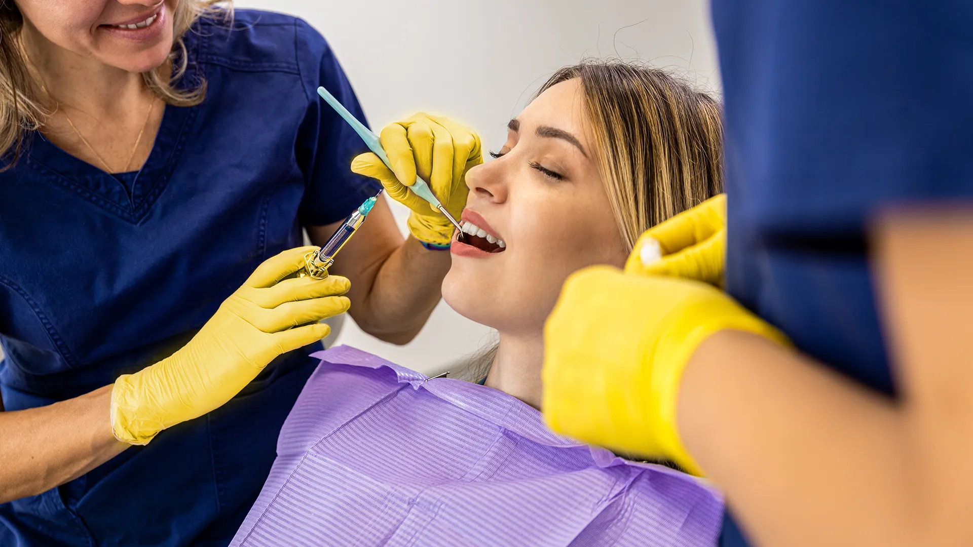 Paciente recostado en el sillón dental con la boca abierta mientras el dentista sostiene una jeringa.