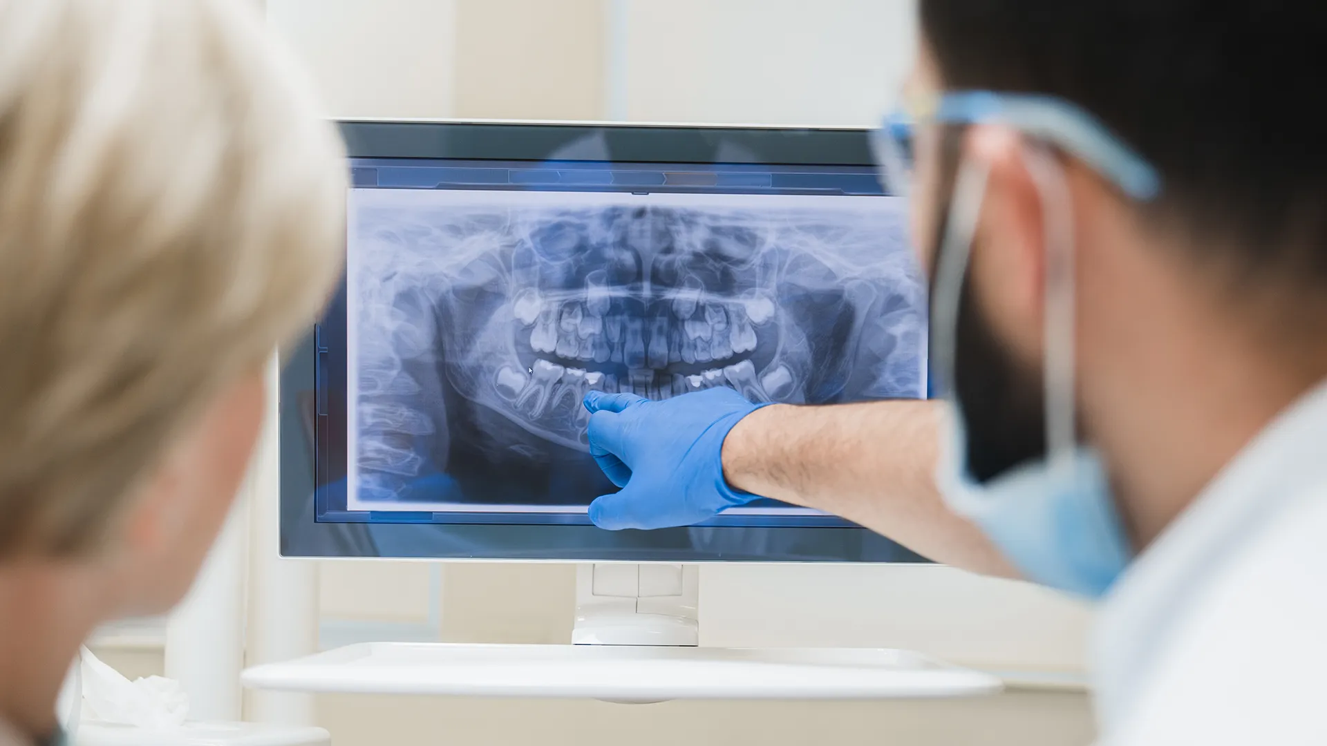 Dentista señalando una pantalla que muestra radiografías dentales.