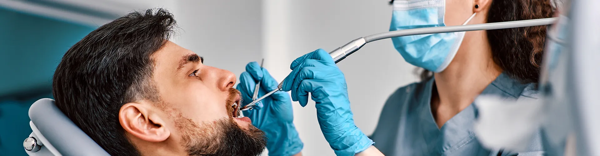 Dentista mujer usando instrumentos dentales en la boca de un paciente masculino.