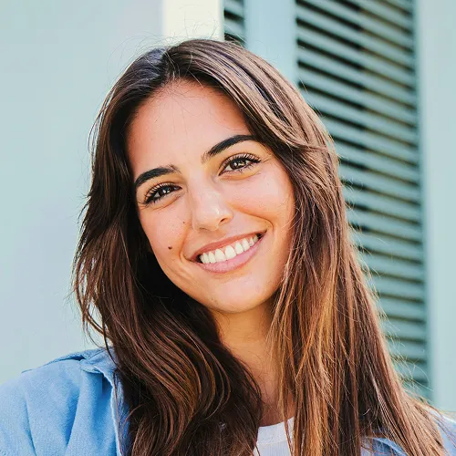 Mujer sonriente de cabello castaño con camisa azul.