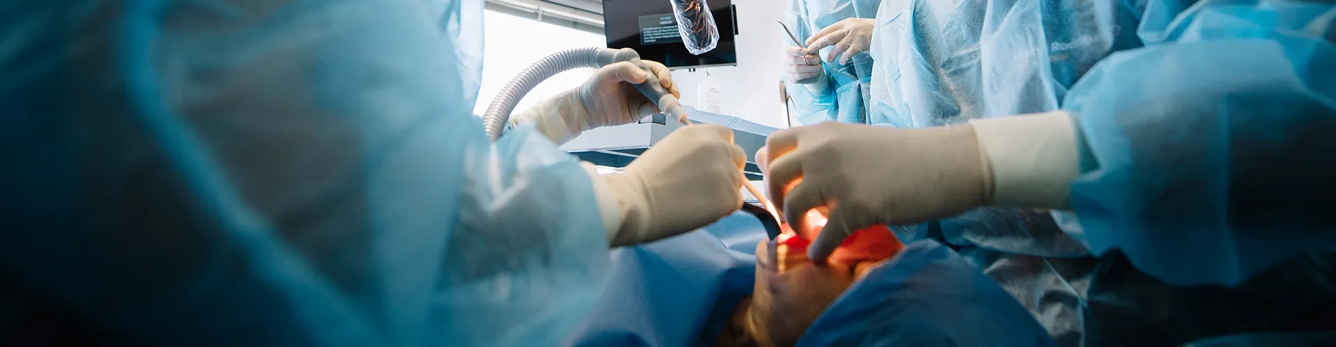 Dos dentistas usando herramientas dentales en la boca de un paciente en una sala de cirugía.