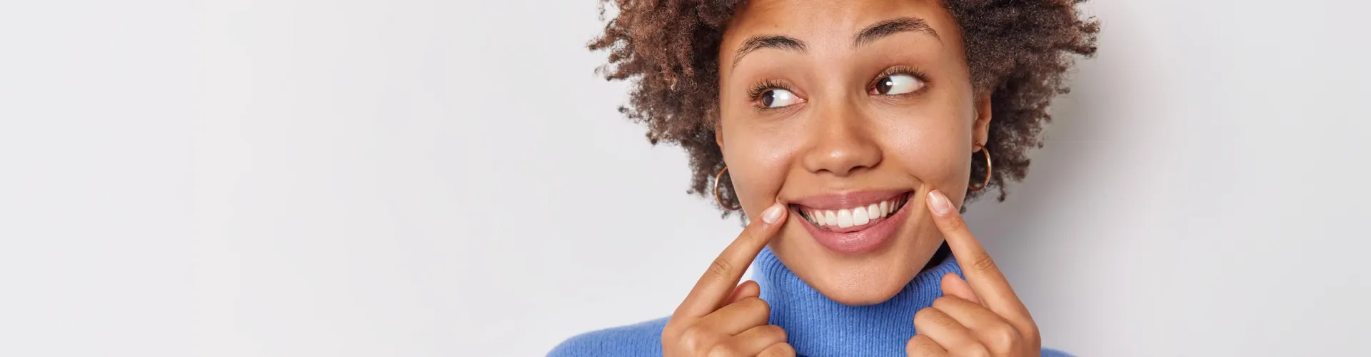 Mujer sonriendo y señalando sus dientes después de un cambio de sonrisa cosmético.