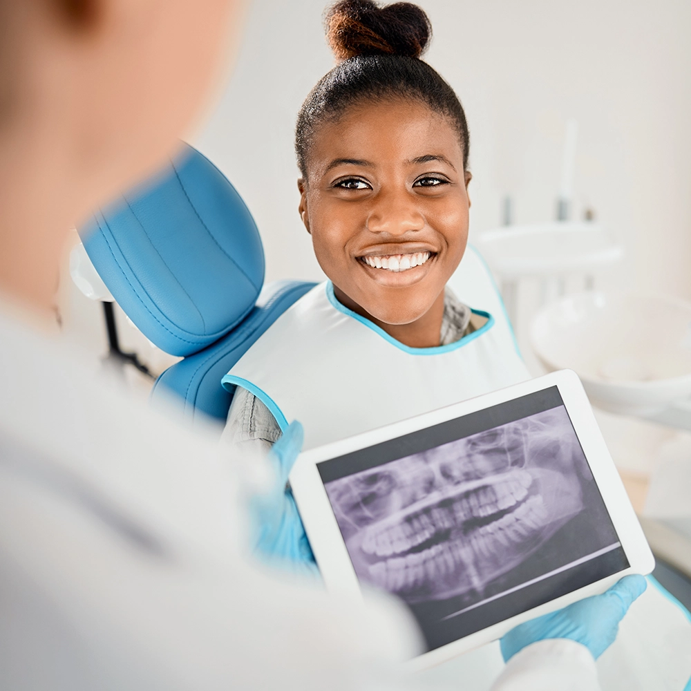 Mujer sentada en el sillón dental sonriendo mientras el dentista sostiene radiografías dentales.