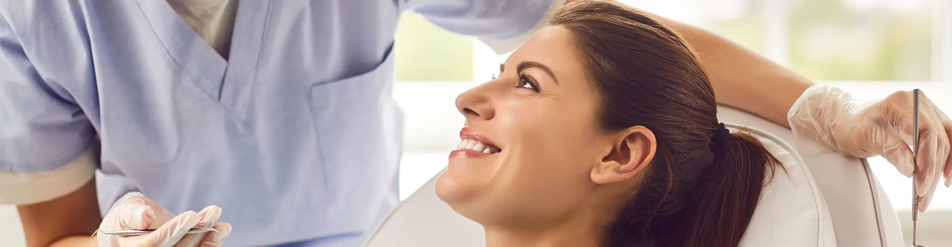Dentista con mascarilla hablando con una mujer sonriente en el sillón dental.