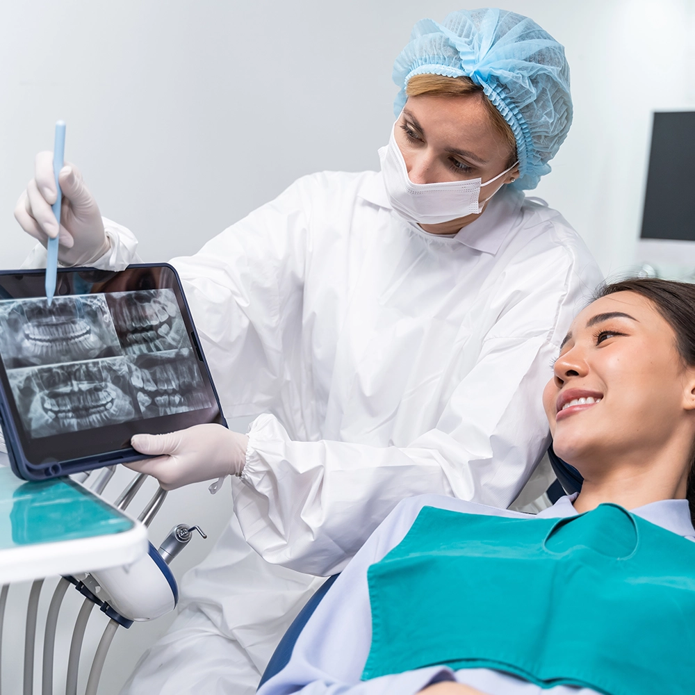 Paciente recostado en el sillón dental mientras el dentista le muestra radiografías dentales.