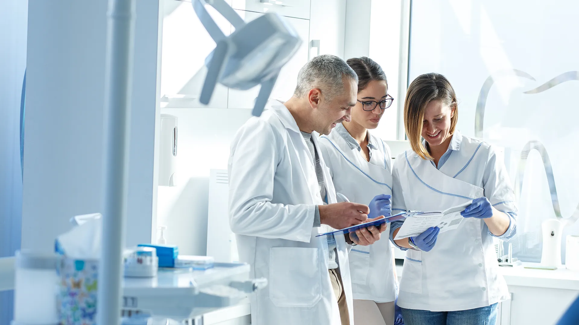 Tres dentistas sonriendo mientras revisan un documento juntos.