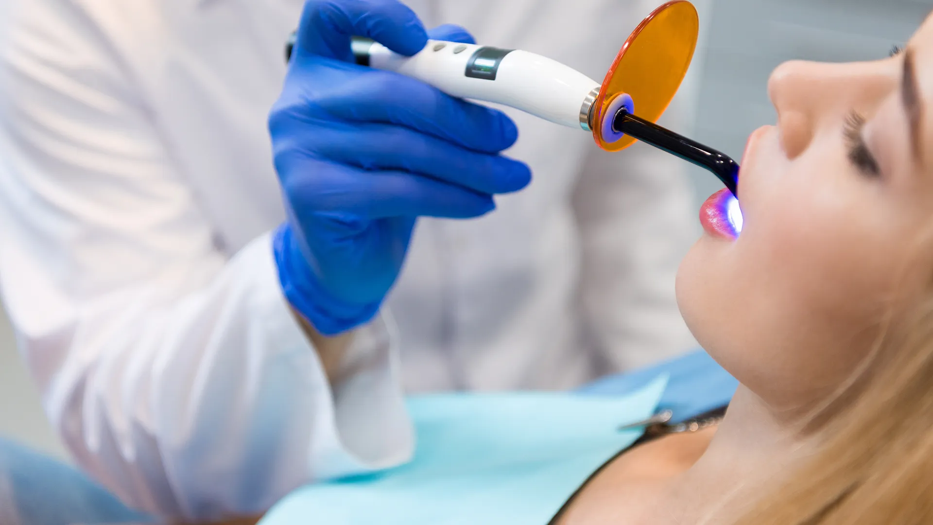 Dentista con guantes azules aplicando luz ultravioleta a los dientes de un paciente.