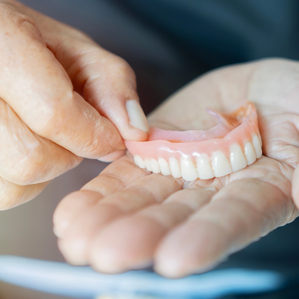 Primer plano de una mano sosteniendo una dentadura inferior, mostrando el diseño detallado y la apariencia natural de los dientes artificiales.