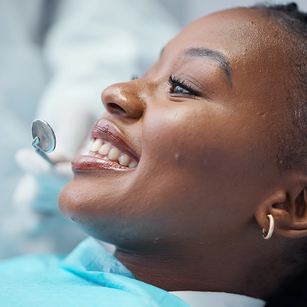 Mujer sonriendo con un espejo dental sostenido frente a sus dientes.
