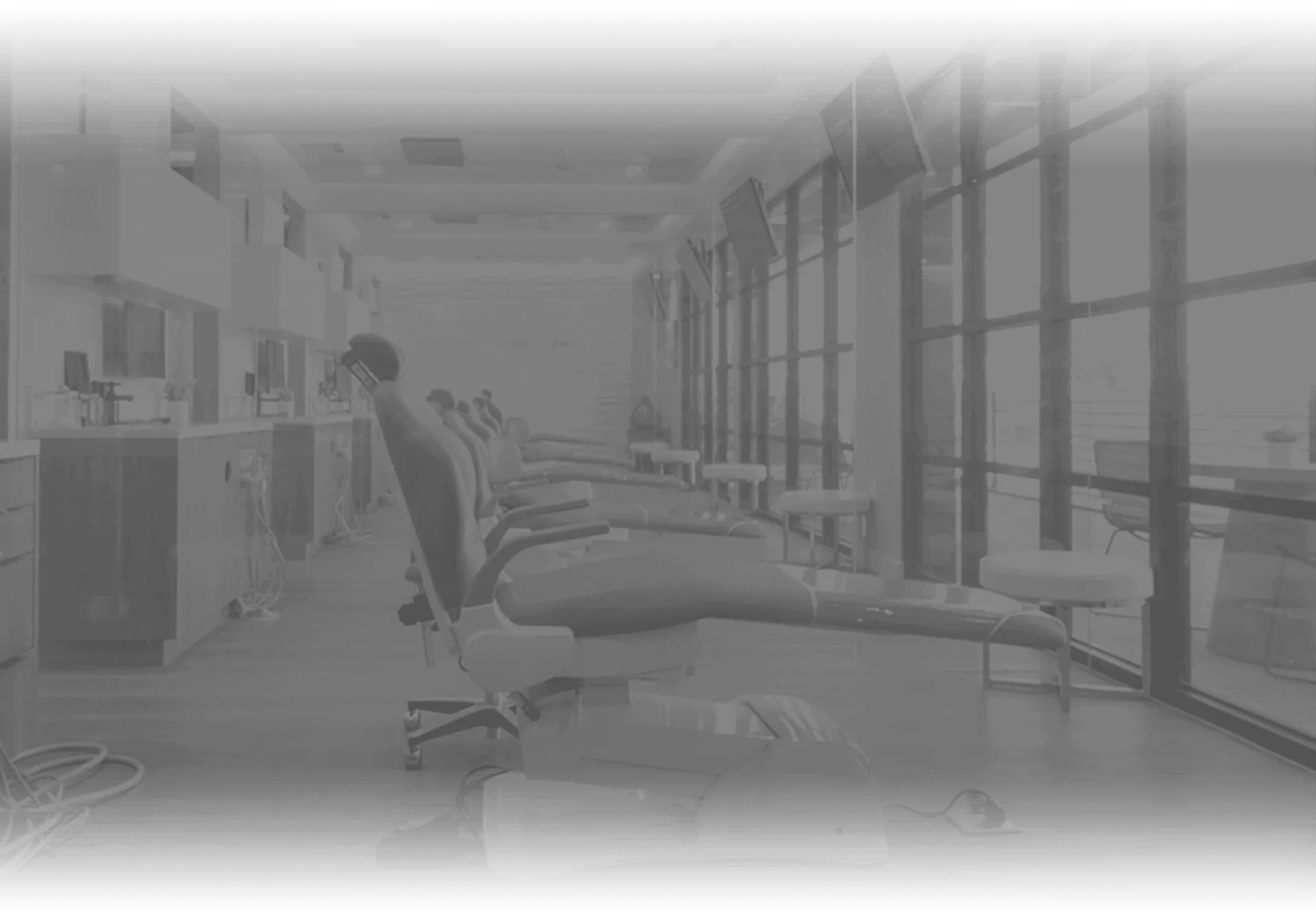 Imagen en escala de grises de un consultorio dental mostrando sillones y equipo dental.