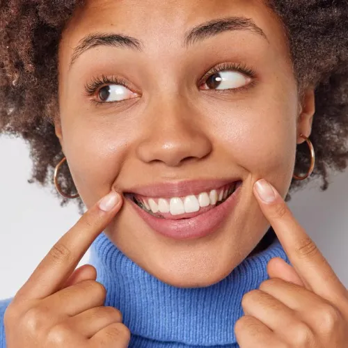 Mujer sonriendo y señalando sus dientes después de un cambio de sonrisa cosmético.