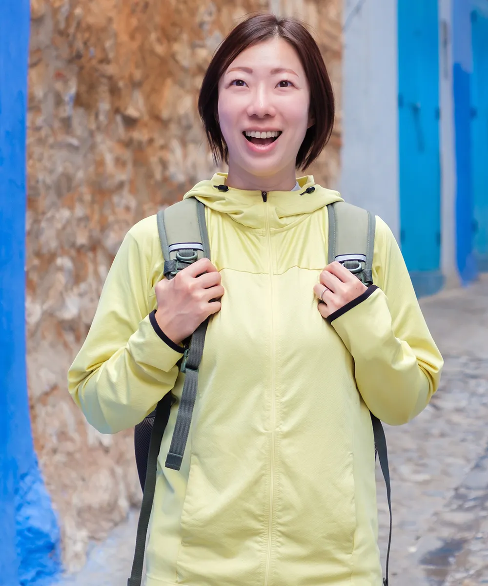 Mujer sonriendo con una mochila puesta, sosteniendo las hombreras con sus manos.