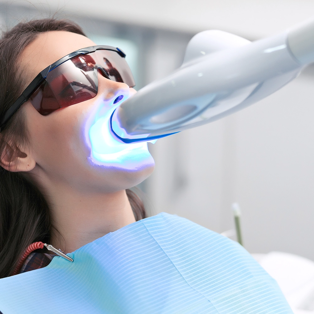 Mujer recibiendo un tratamiento de blanqueamiento dental con luz ultravioleta mientras lleva gafas protectoras.