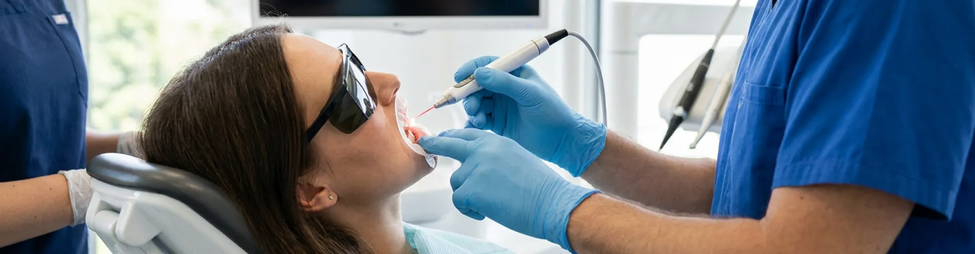 Paciente sometiéndose un tratamiento de contorneado de encías con láser mientras usa gafas protectoras, mientras el dentista remodela cuidadosamente la línea de las encías para mejorar la estética de la sonrisa y la salud bucal.