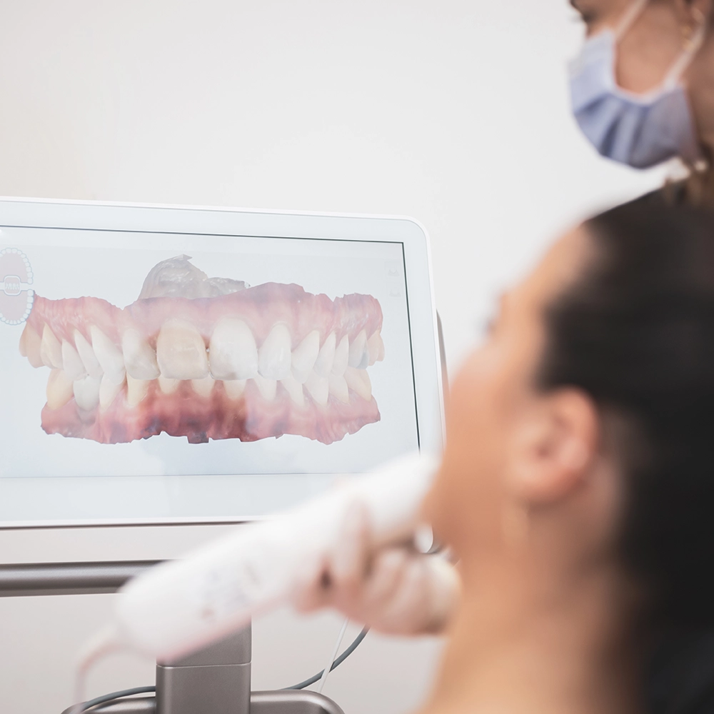 Mujer sentada en el sillón dental viendo una imagen 3D de sus dientes en una pantalla.
