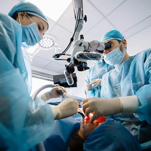 Dos dentistas usando herramientas dentales en la boca de un paciente en una sala de cirugía.