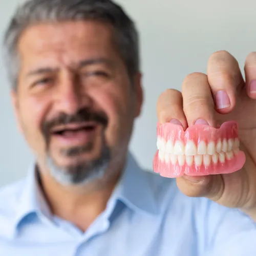 Hombre sonriente sin dientes sosteniendo dentadura superior e inferior.