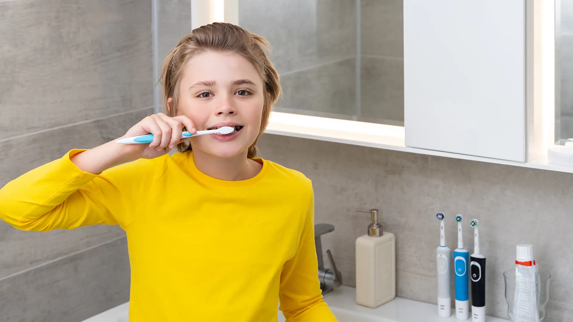 Niño con suéter amarillo cepillándose los dientes mientras mira a la cámara.