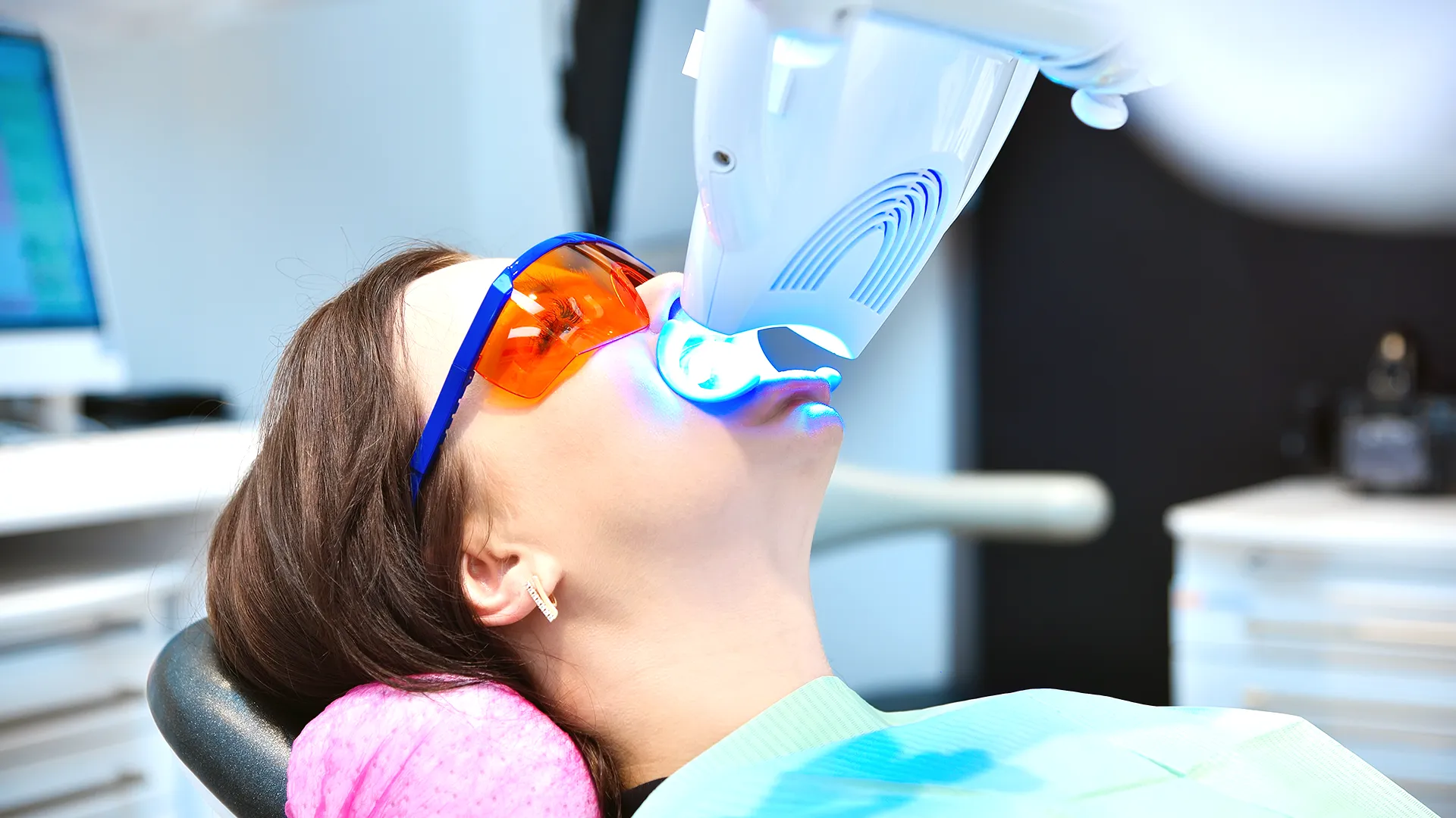 Mujer recibiendo un tratamiento de blanqueamiento dental con luz ultravioleta mientras usa gafas protectoras.